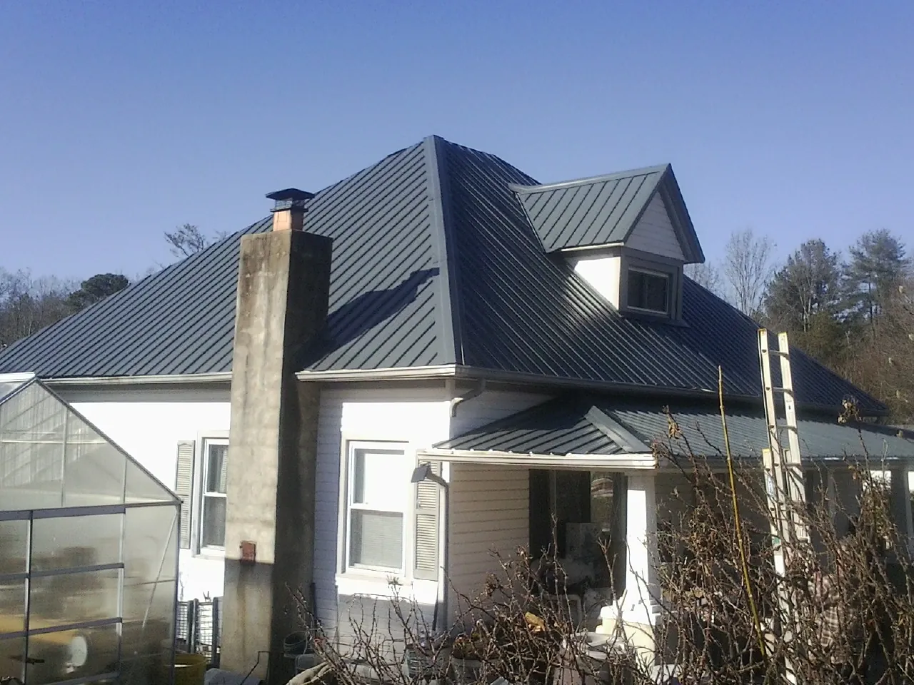 Dark blue standing seam metal roof on a white farmhouse with dormer — Slate & Tile Roof Repair by Roofing Brothers in Hart