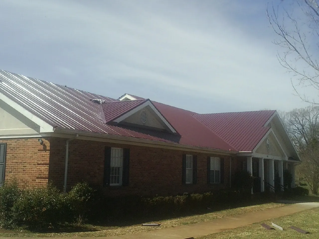 Red metal roof with gabled entries on a long brick building, from a Hail Damage Roof Repair job in Hart