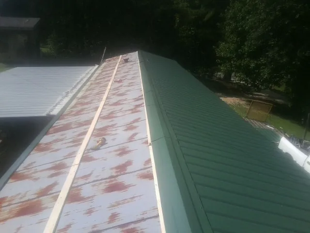 Old rusted panels beside newly installed green metal roofing — Wind Damage Roof Repair by Roofing Brothers in Hart