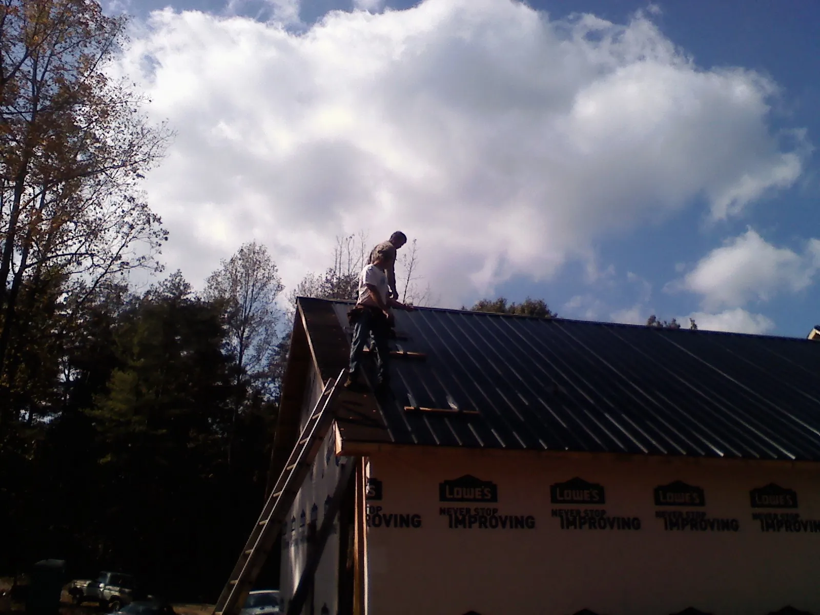 Roofer fastening dark metal panels high against a cloudy sky, from a Roof Inspection job in Hart