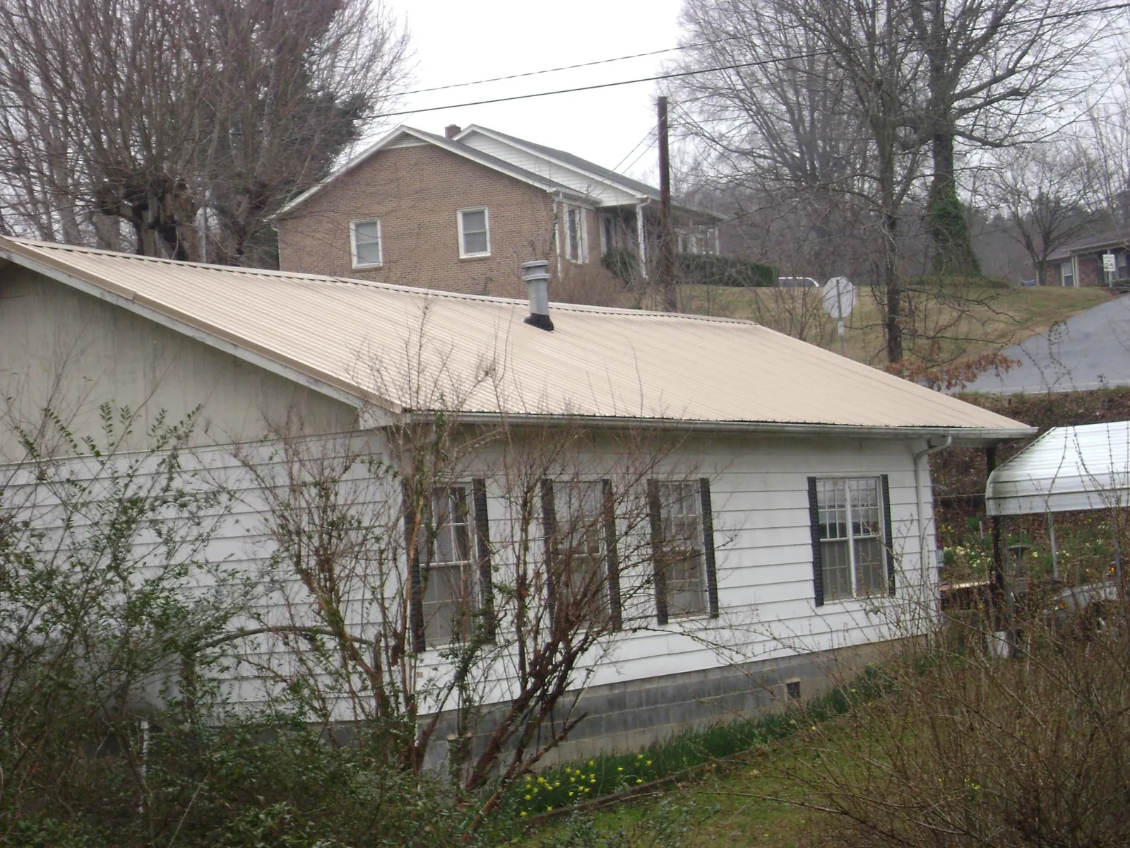 Tan metal roof on a white sided house set into a hillside — Commercial Roofing by Roofing Brothers in Hart