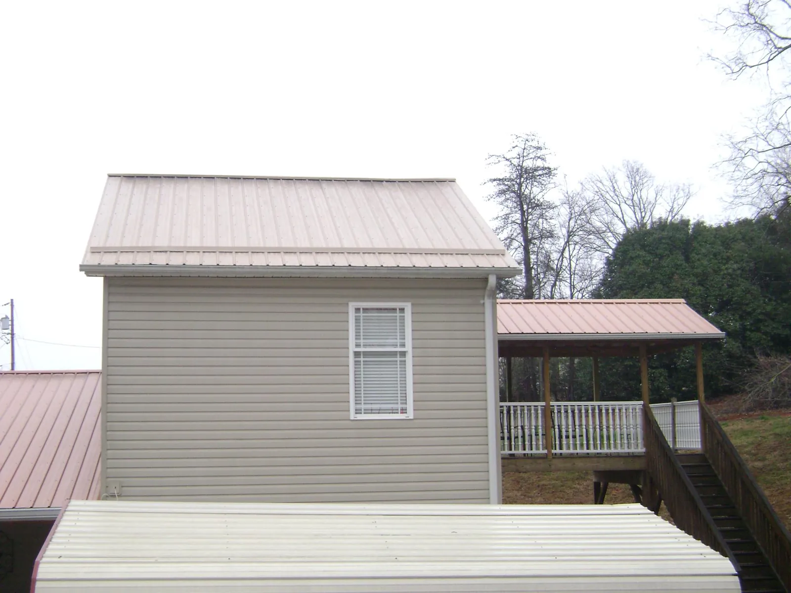 Tan metal roofs on a two story addition and attached porch, from a Roof Replacement job in Hart