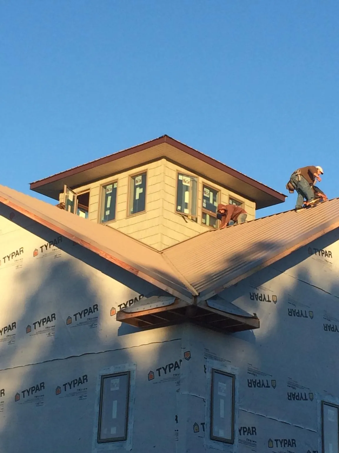 Roofers working around a rooftop cupola on a new metal roof at sunset — Roof Waterproofing in Hart by Roofing Brothers